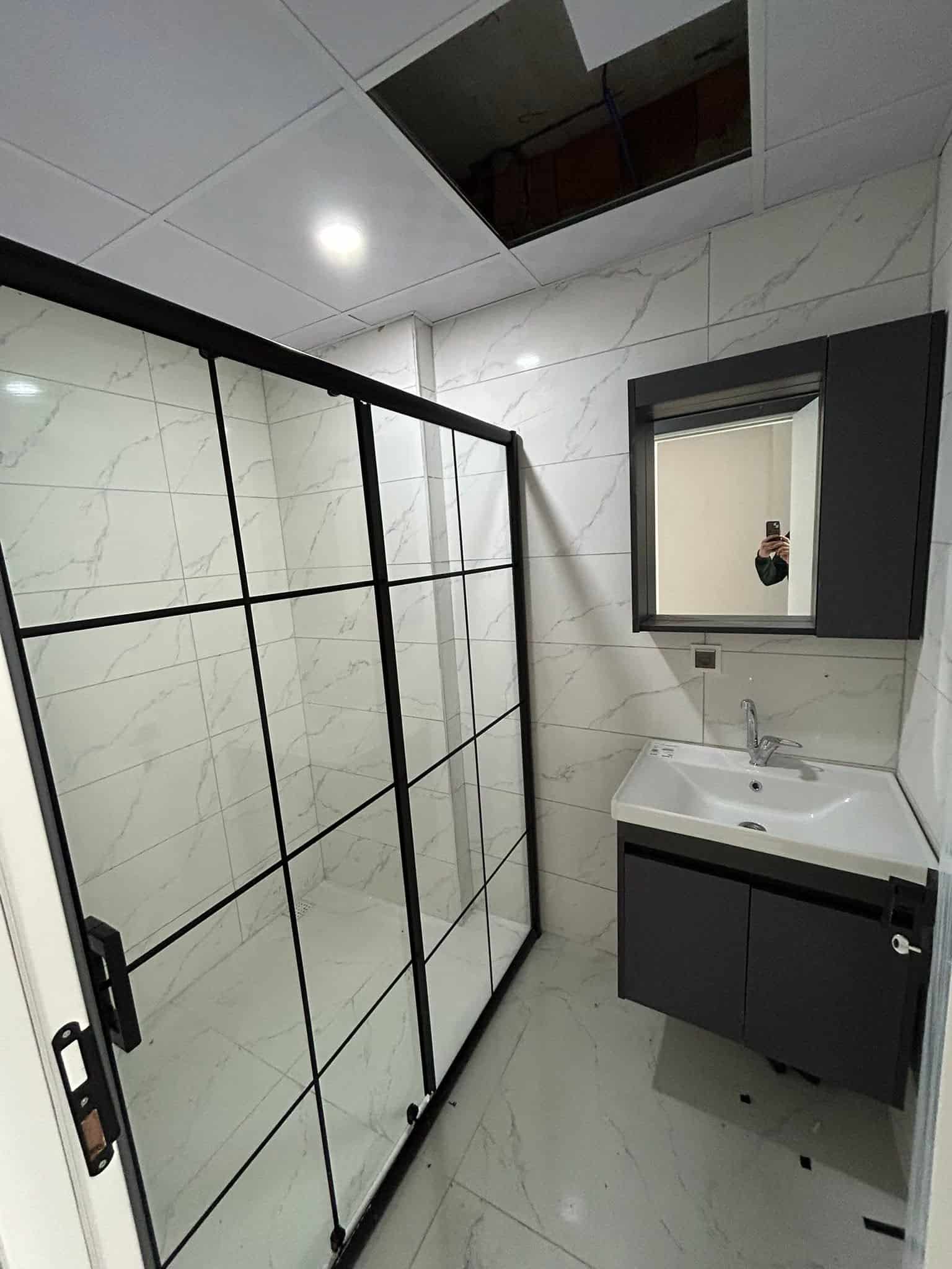 Siyah çerçeveli duş kabini ve lavabo alanı